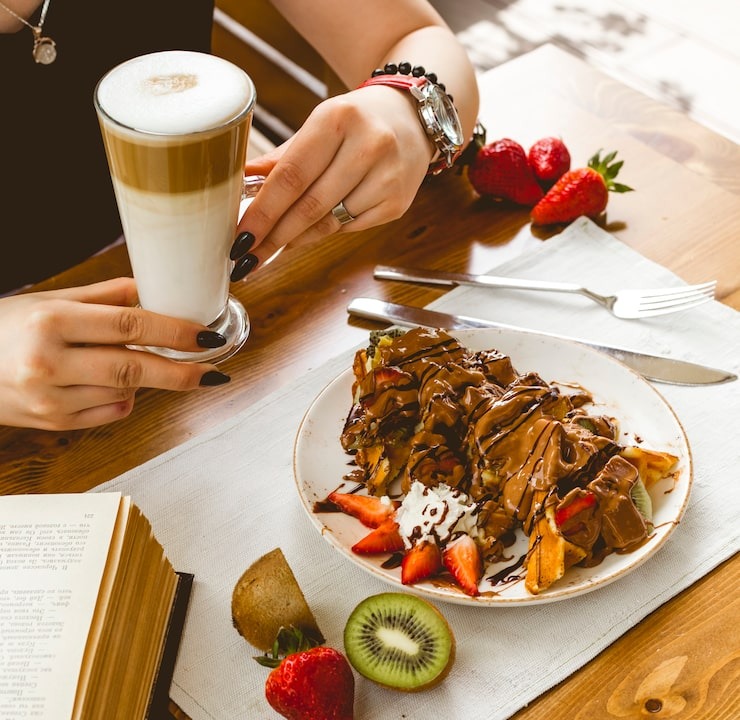 Gourmet waffles topped with chocolate drizzle, fresh strawberries, and kiwi served with an iced latte coffee.