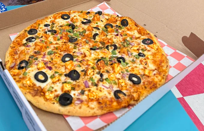 Handmade specialty takeaway pizza topped with black olives, paneer, and red onions from Cool Flames Cafe.